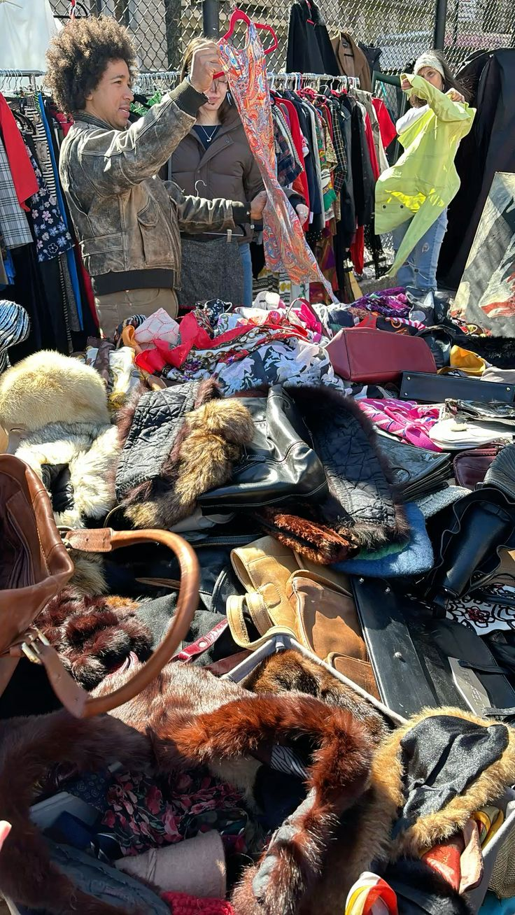 An open-air second-hand clothing sale with racks of vintage garments and shoppers browsing